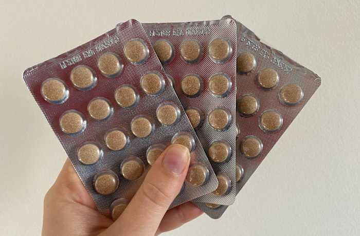 A person holding three sheets of Viviscal Hair Growth supplement tablets against a white background.